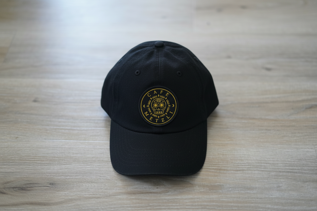 A brown baseball cap with the 'Café Metzli' logo patch on the front.